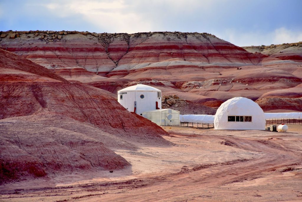 Desert scene featuring remote Mars research station against rugged red hills.