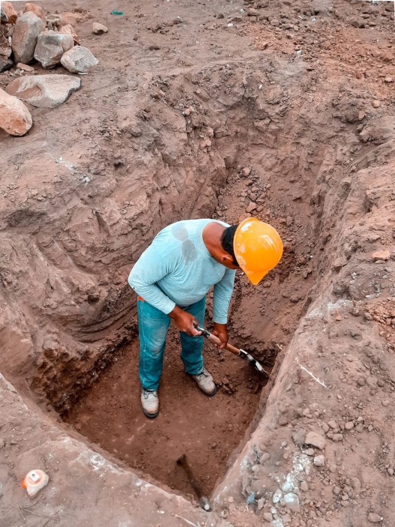 A construction worker in safety gear digs at a site in Lambayeque, Perú, showcasing manual labor and construction processes.