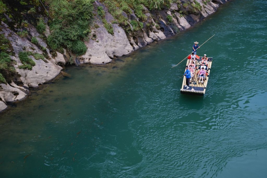 A group enjoying a serene bamboo raft ride on a turquoise river beside lush green cliffs.