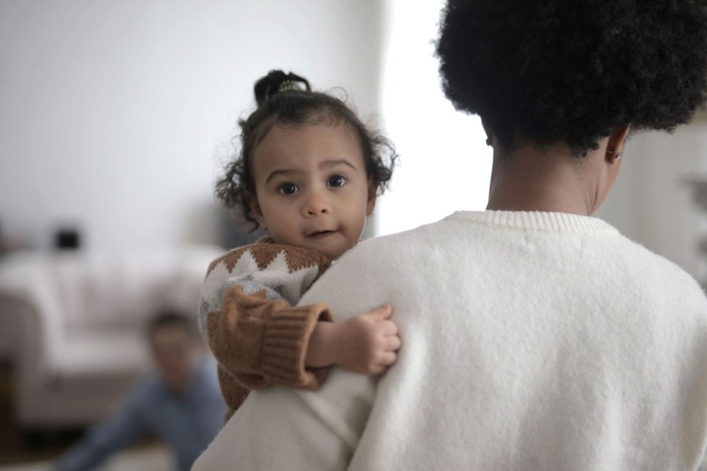 A toddler is lovingly held by a parent indoors, depicting warmth and togetherness.