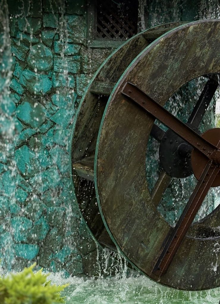 Close-up of a rustic water wheel with flowing water, picturesque setting.