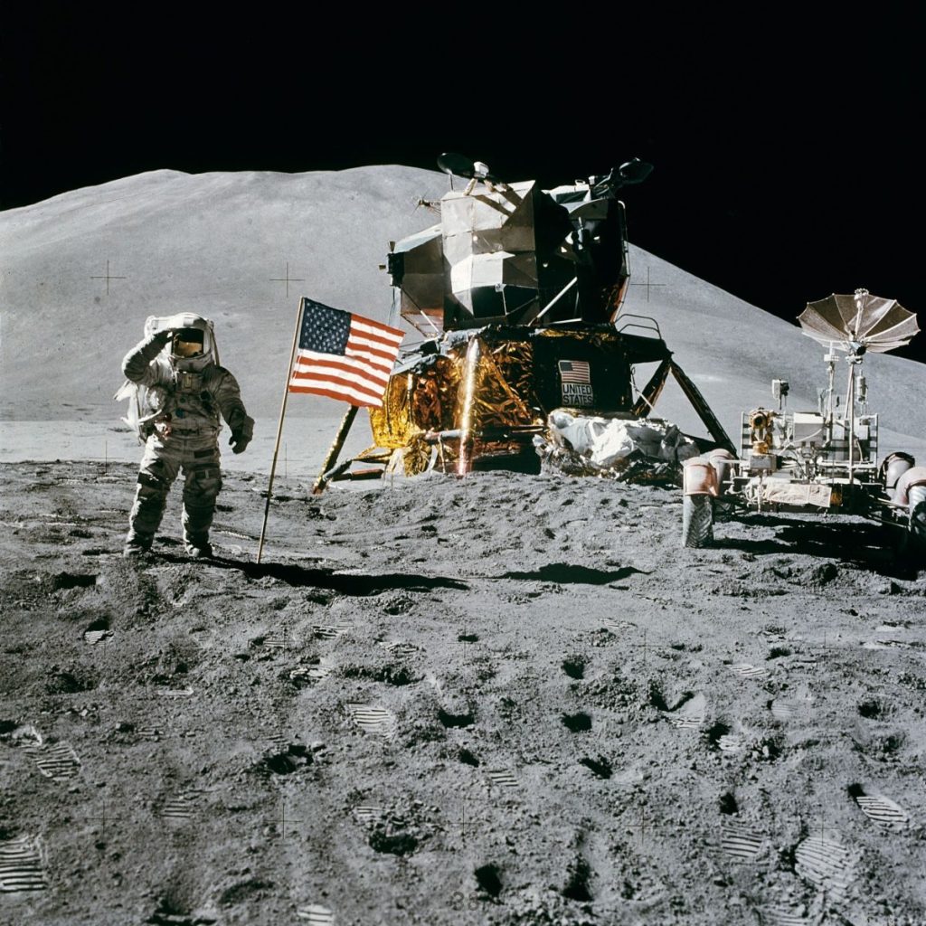 Astronaut on the moon near lunar module and American flag during historic landing.