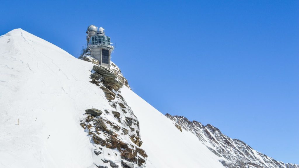From below of observation tower on rough snowy ridge under colorful cloudless sky in winter