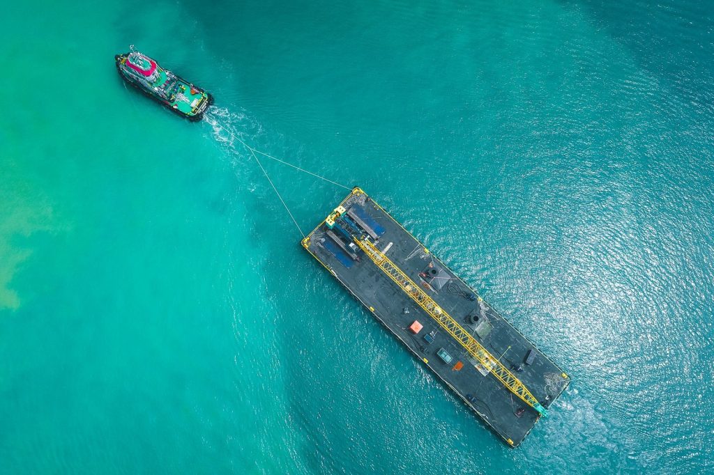 Drone view of contemporary powerful boat pulling swimming platform with crane along blue calm seawater