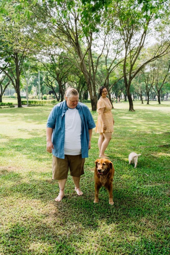 Two adults enjoying a sunny day in the park with a Golden Retriever and a small dog.