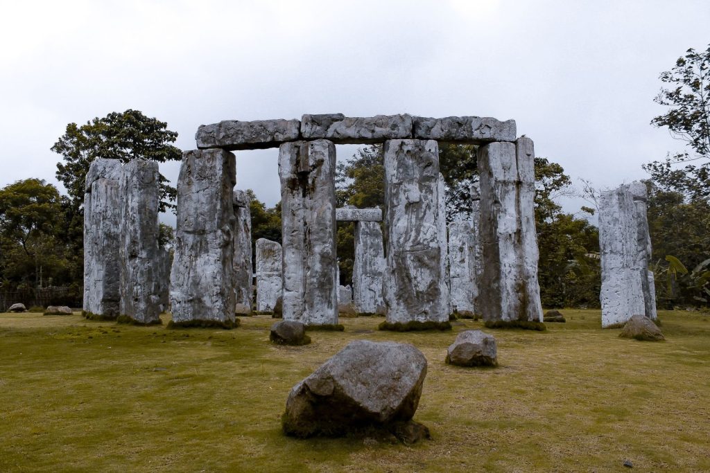 Replica stone structure resembling Stonehenge in a grassy outdoor setting with overcast skies.