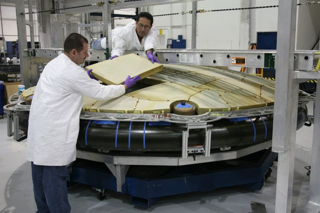 Concentrated male mechanics in protective uniform assembling detail of large spacecraft component at modern factory