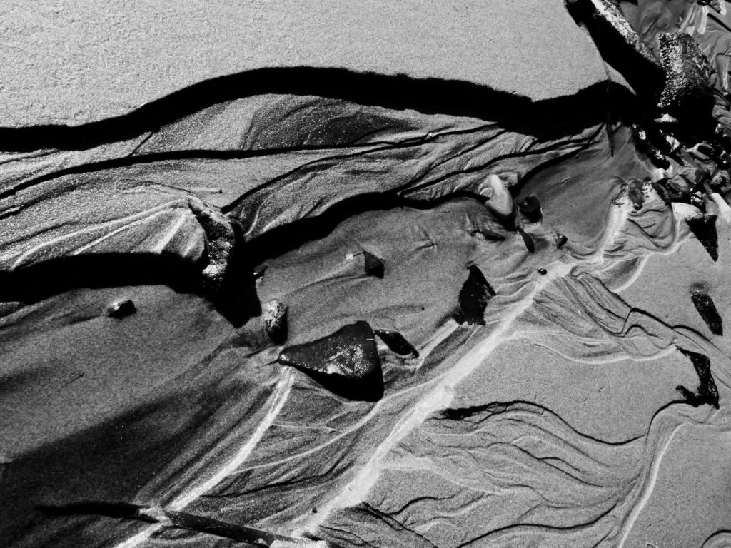 Captivating aerial view of abstract sand patterns on a seashore in black and white.