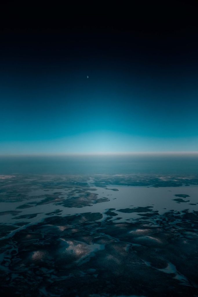 Breathtaking scenery of snowy mountain ridge from airplane window flying in cloudless blue sky in evening