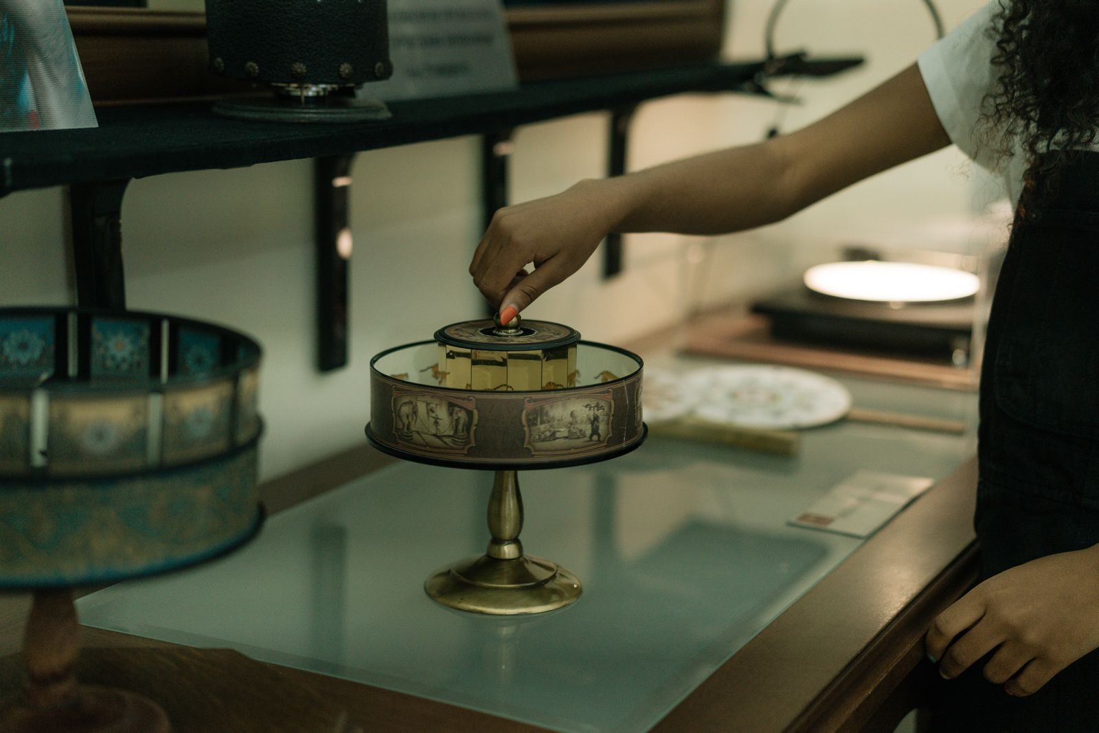 A person interacts with a vintage zoetrope displayed indoors, capturing a moment of curiosity.