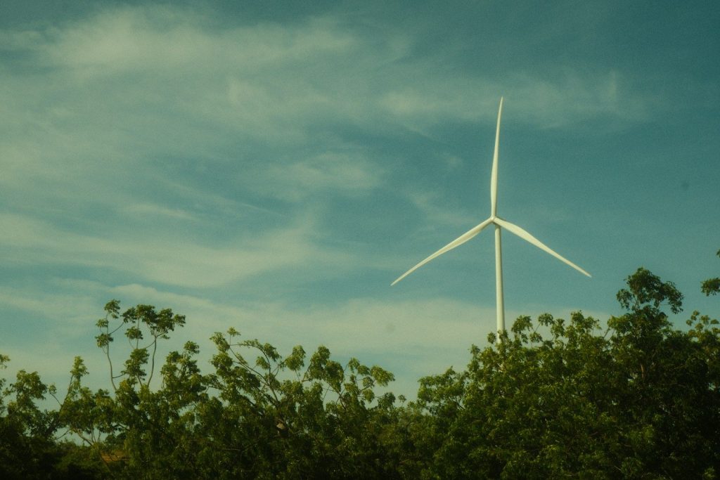 A wind turbine with green trees and a blue sky.