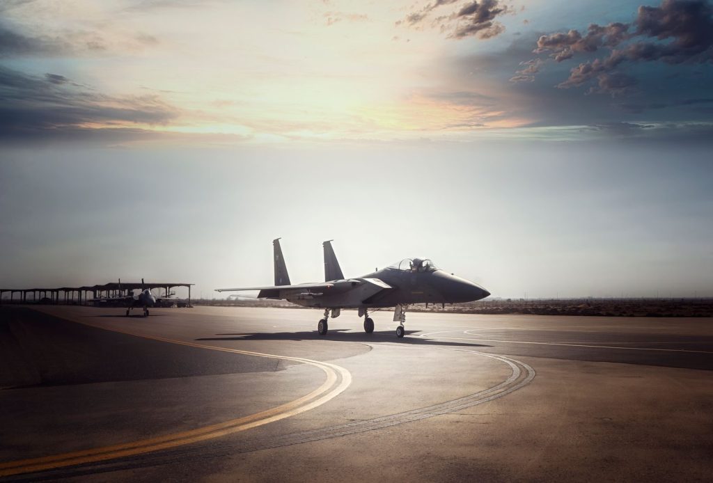 A military fighter jet prepares for takeoff on a runway during sunrise.