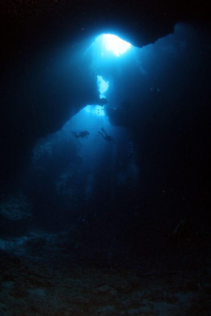 Divers explore a stunning underwater cave with dramatic light rays filtering through.