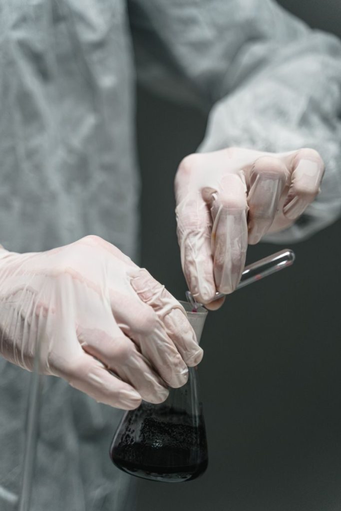 Close-up of a scientist with gloves holding a flask and test tube in a lab setting.
