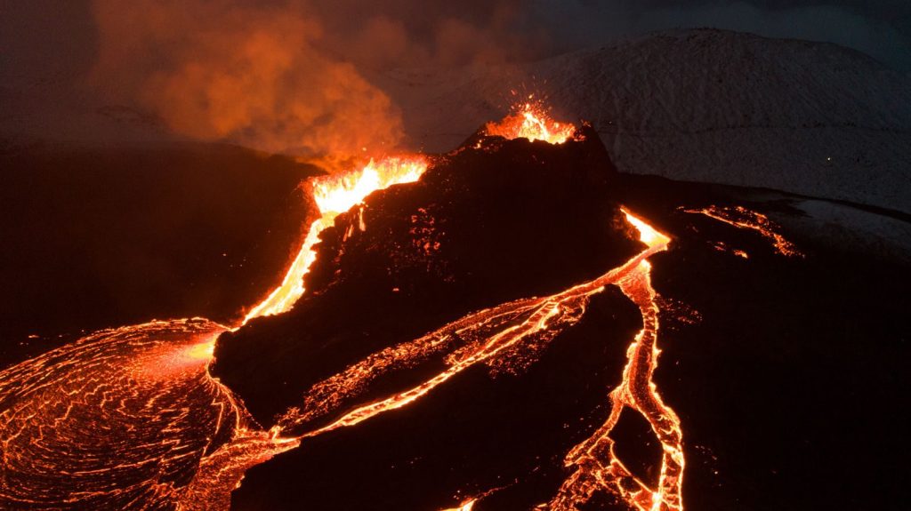 Captivating aerial view of a volcano eruption with flowing lava under the night sky.