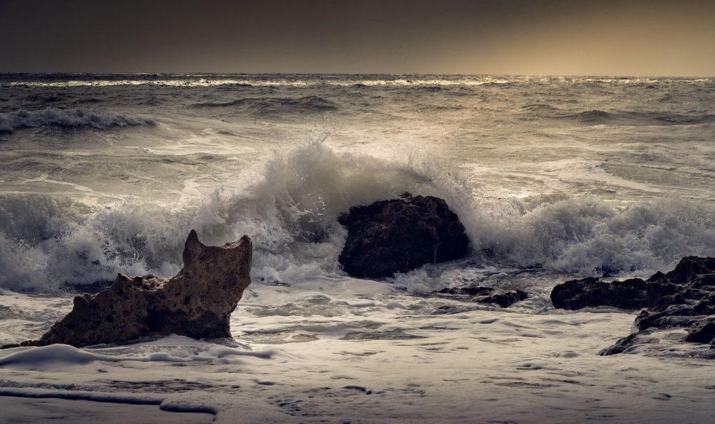 Powerful ocean waves crash onto rugged rocks under a moody sky.