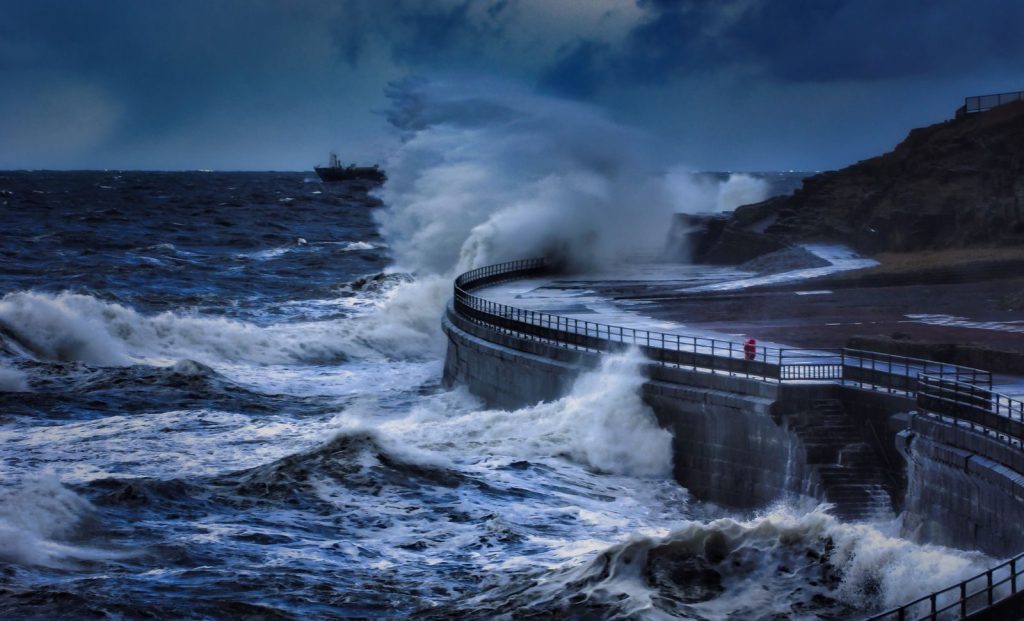 Powerful ocean waves crash against a concrete seawall during a storm.