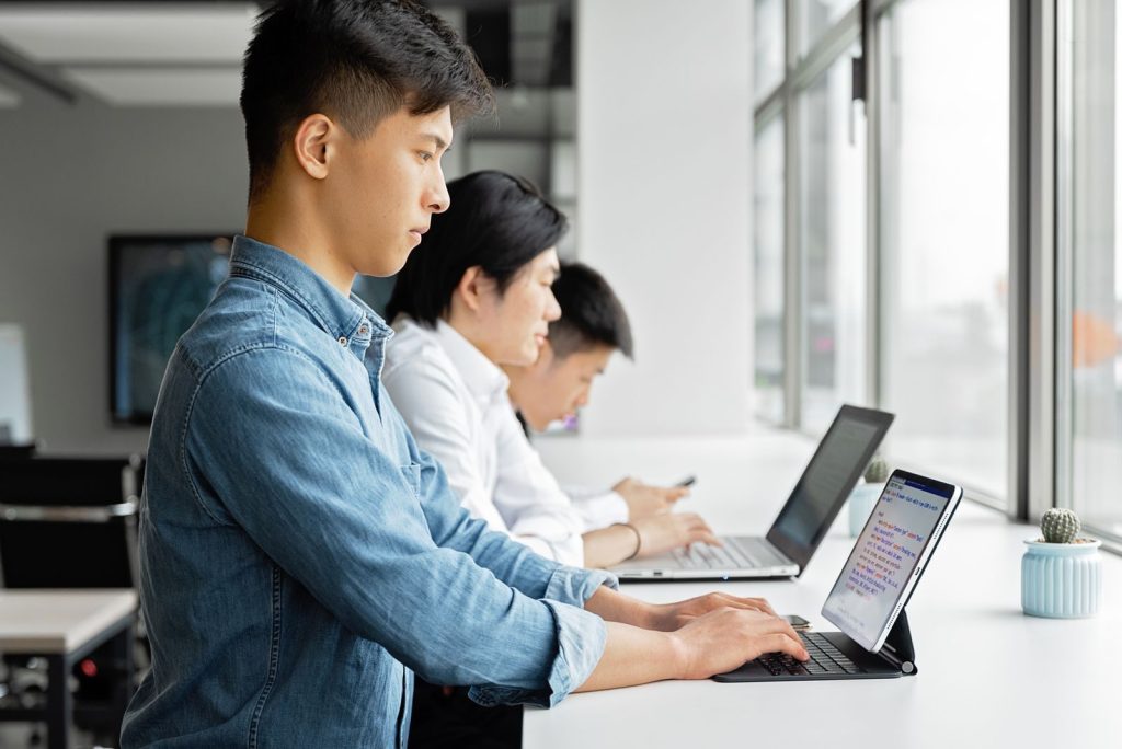 A group of young professionals working with laptops in a bright, modern office setting.