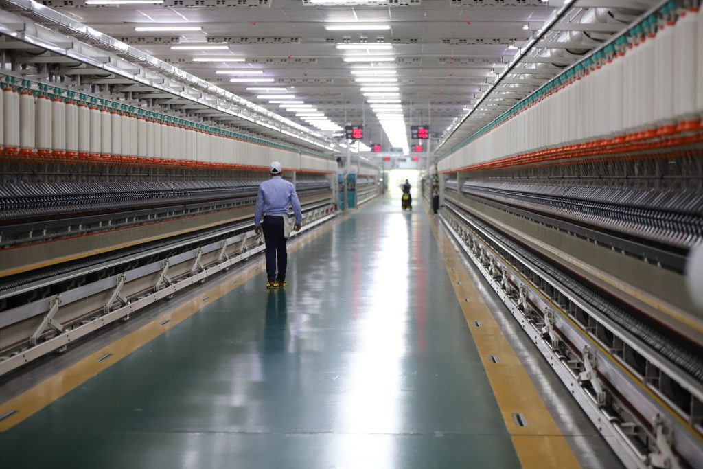 A man walks through a well-lit hallway in a modern industrial textile plant in India.