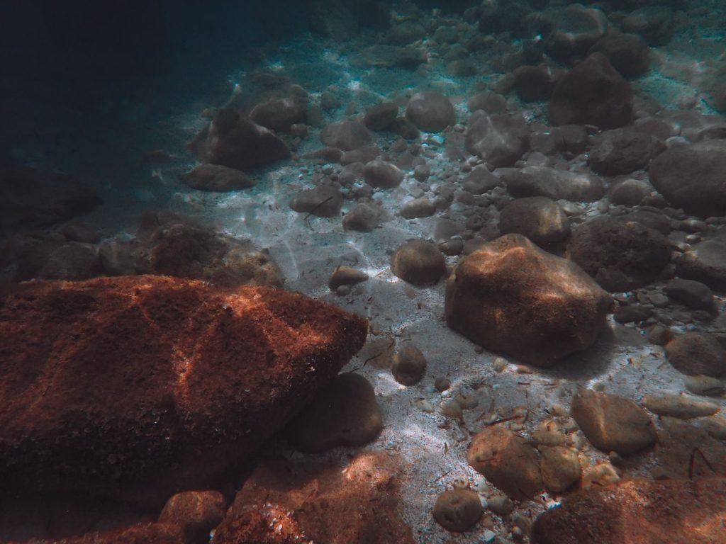 A serene view of rocks and sunlight patterns underwater, showcasing natural beauty.