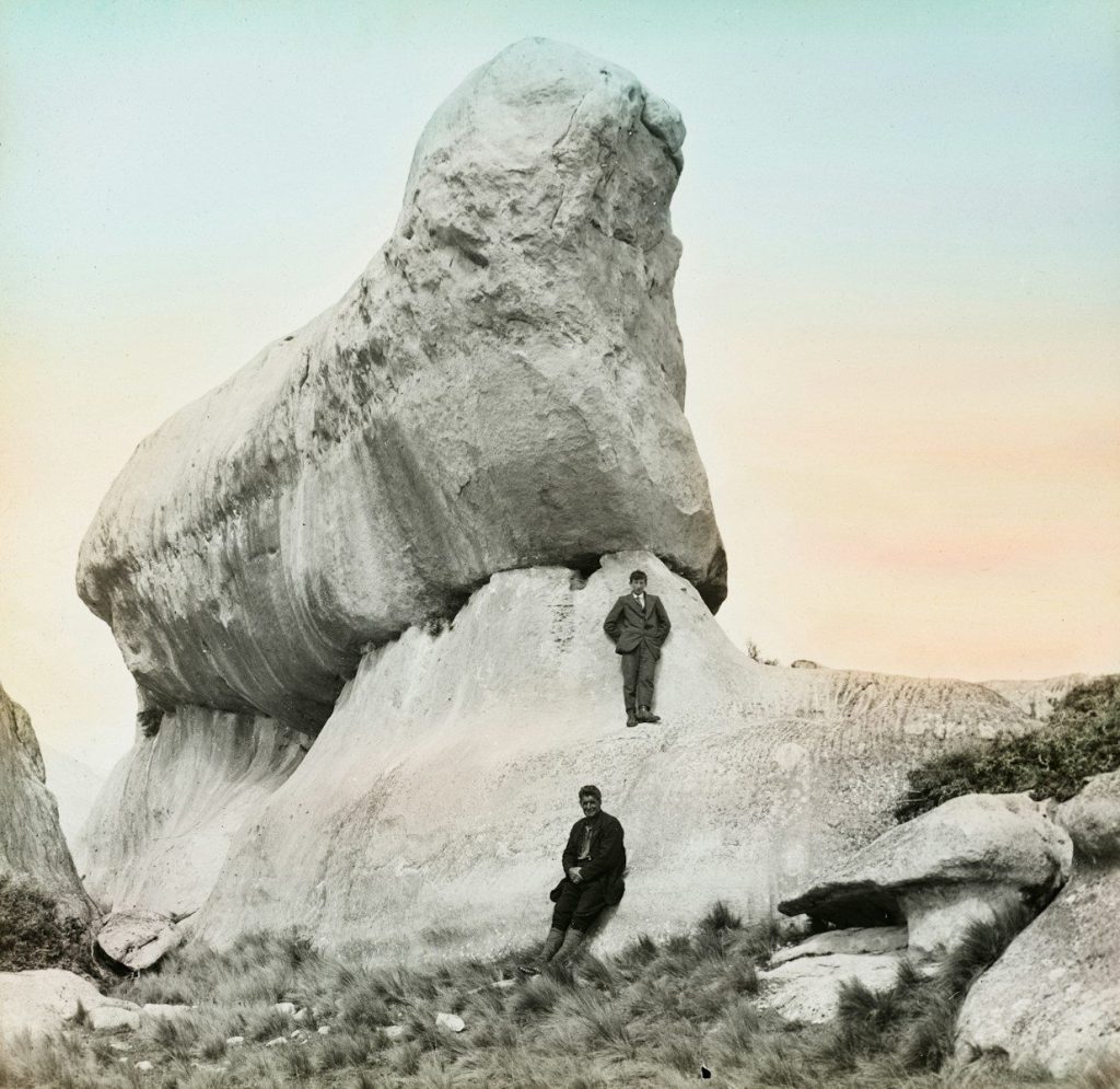 Two men stand near a large, weathered rock formation.