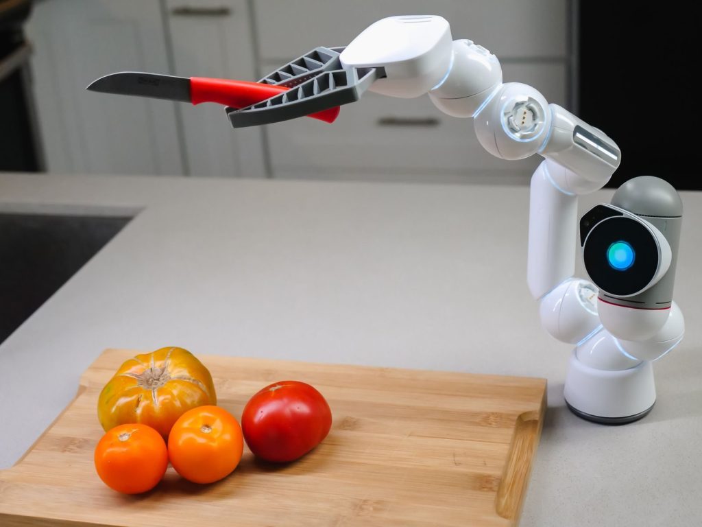A futuristic robotic arm with a knife preparing colorful tomatoes in a modern kitchen.