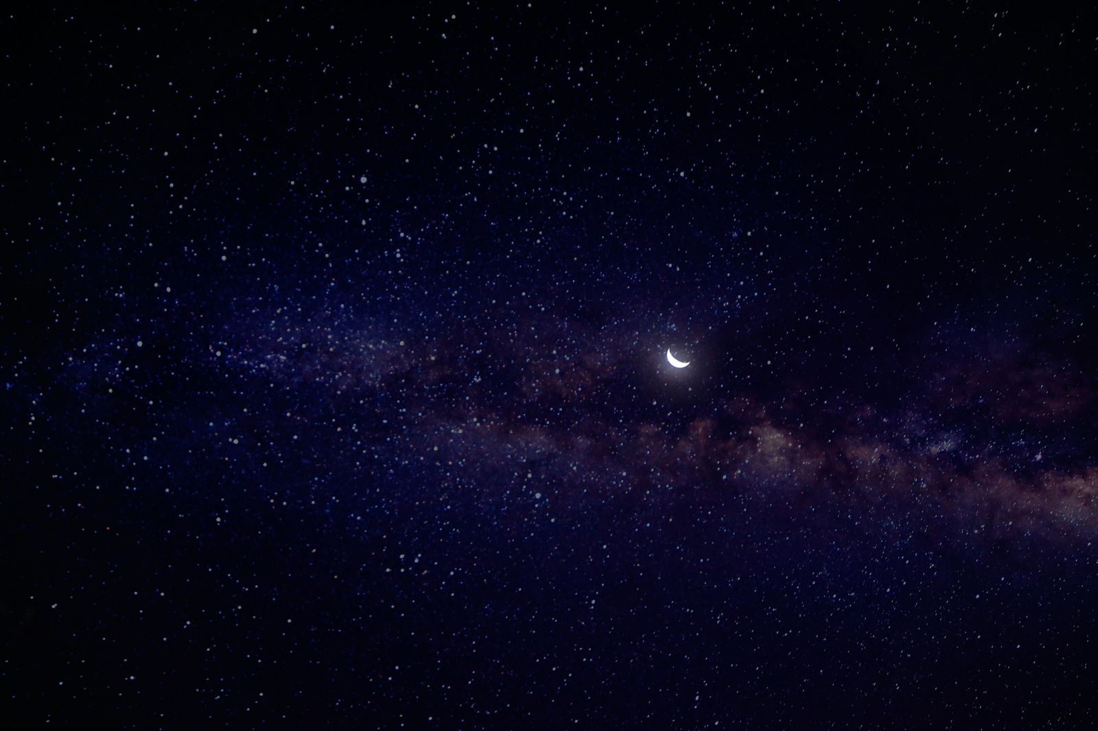 A serene view of a crescent moon nestled in a star-filled night sky with the Milky Way.