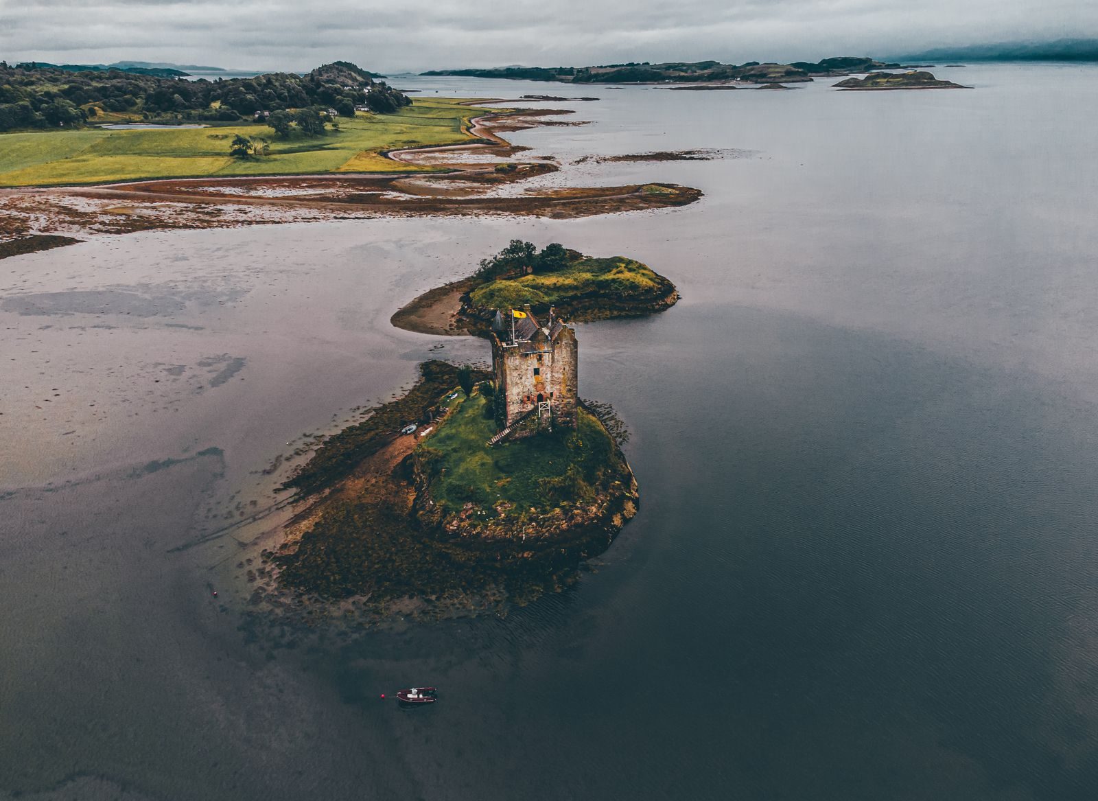 Aerial shot of Castle Stalker on Loch Laich, depicting a moody landscape in Argyll and Bute, Scotland.