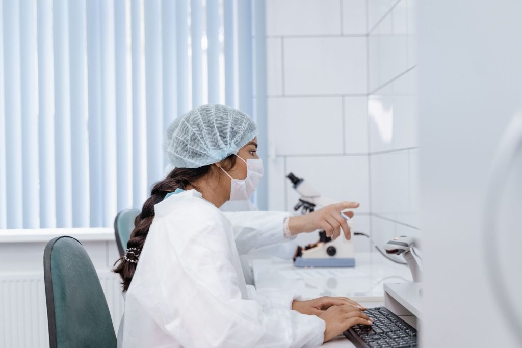 Female scientist in laboratory coat working at computer in a clean, modern lab.
