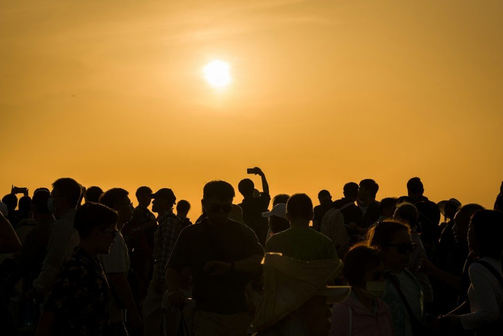 Silhouetted crowd watches the sun setting over the horizon.
