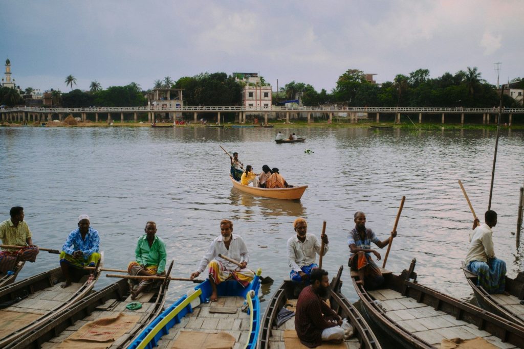Men sit in boats on a river with a bridge.