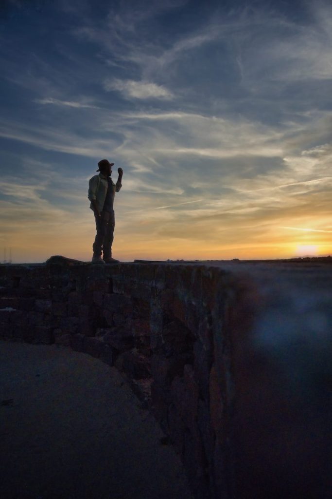 a man standing on top of a cliff at sunset