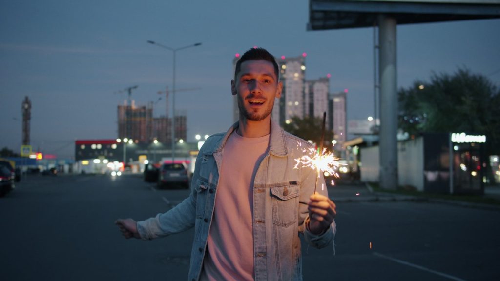 Man holding sparkler on street at dusk