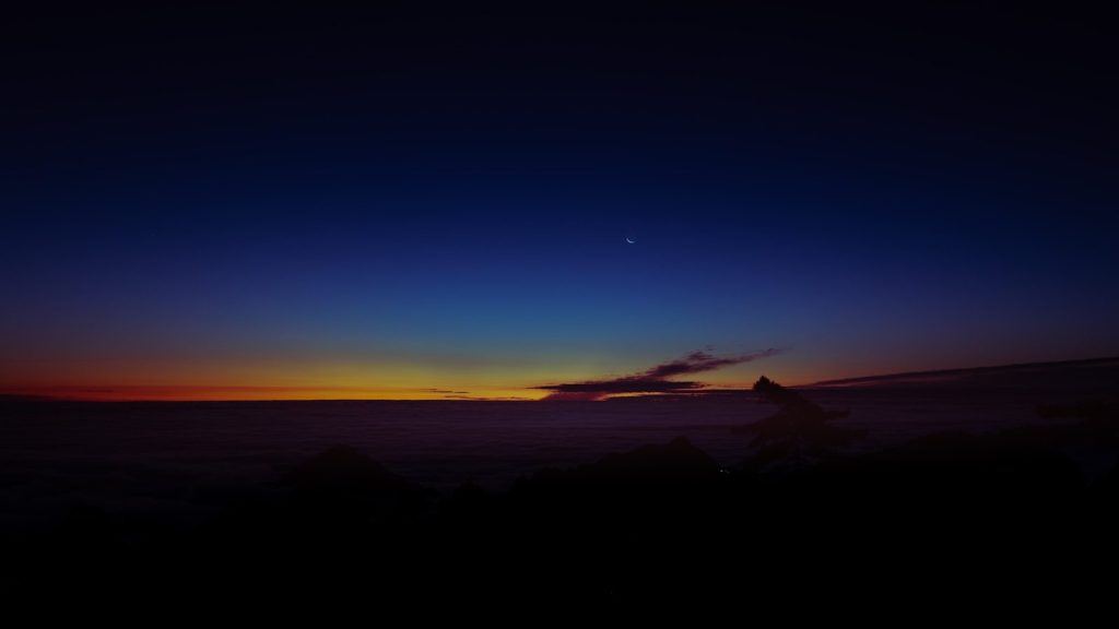 Deep blue and orange twilight sky over silhouetted landscape.