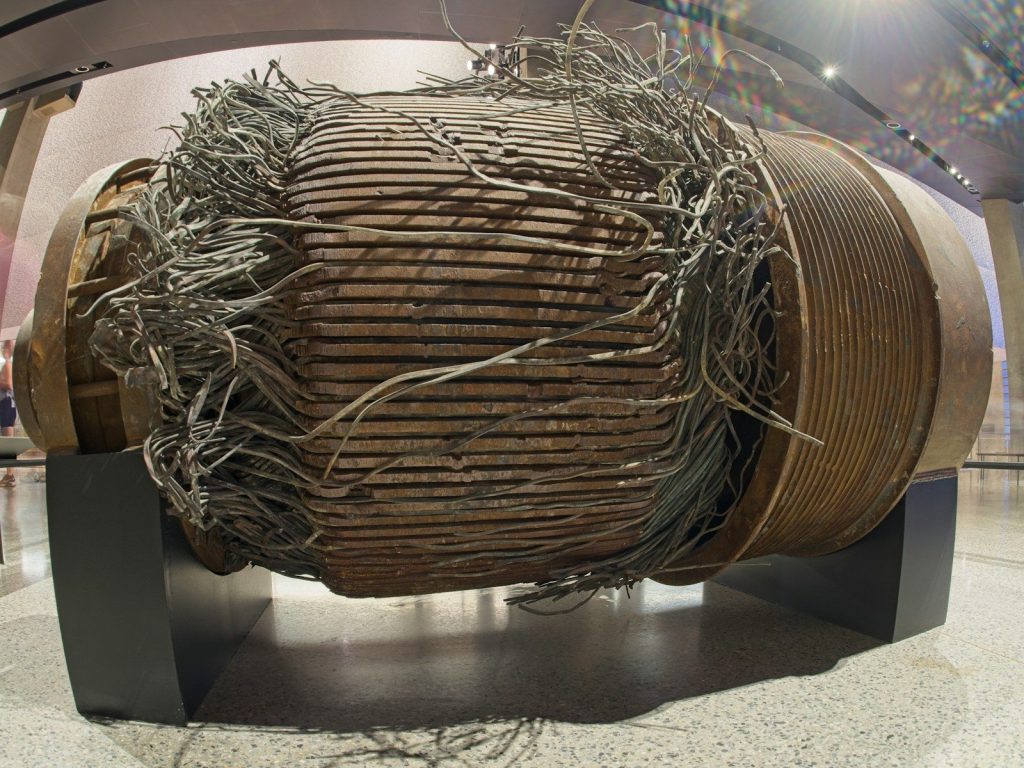 A large, damaged industrial coil with tangled wires on display.