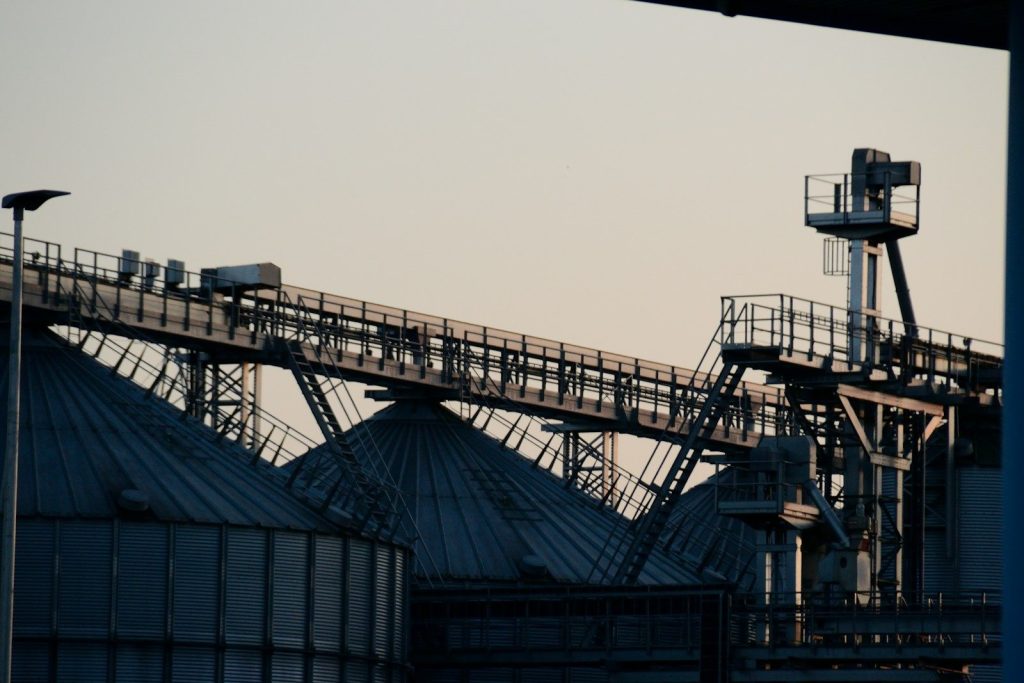 Industrial silos and conveyor belts against a pale sky.
