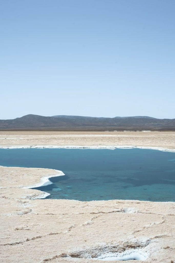 A bright blue pool of water surrounded by salt flats.