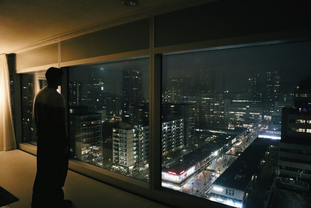 a man looking out a window at a city at night