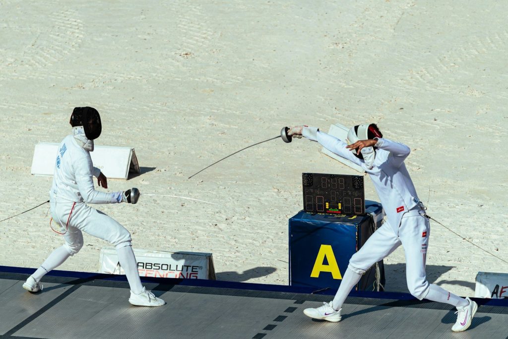 Two fencers in white uniforms engaged in a fencing match.