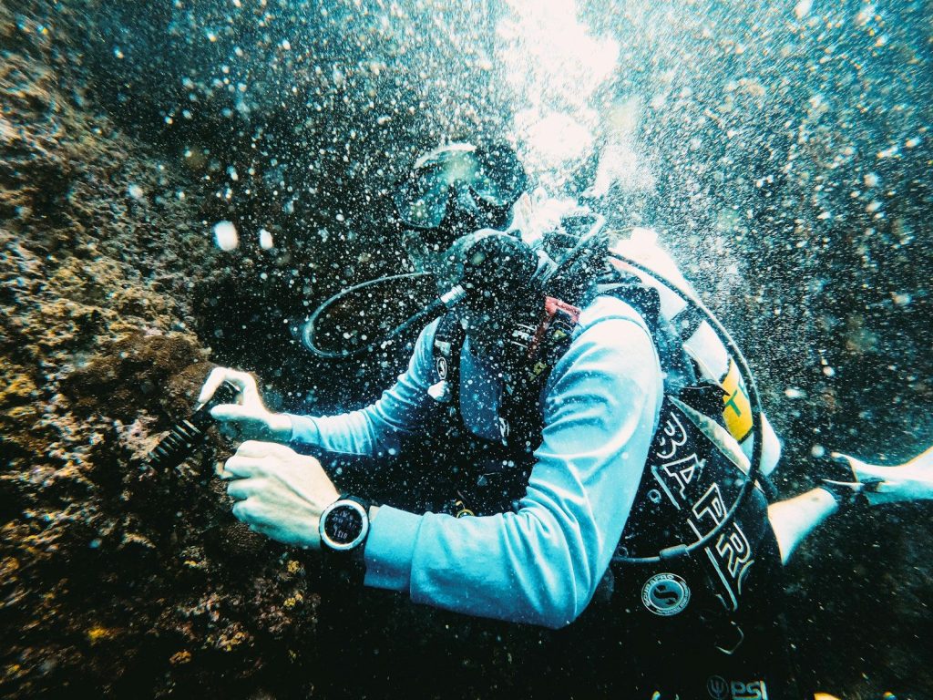 Scuba diver explores underwater rock formation with bubbles.
