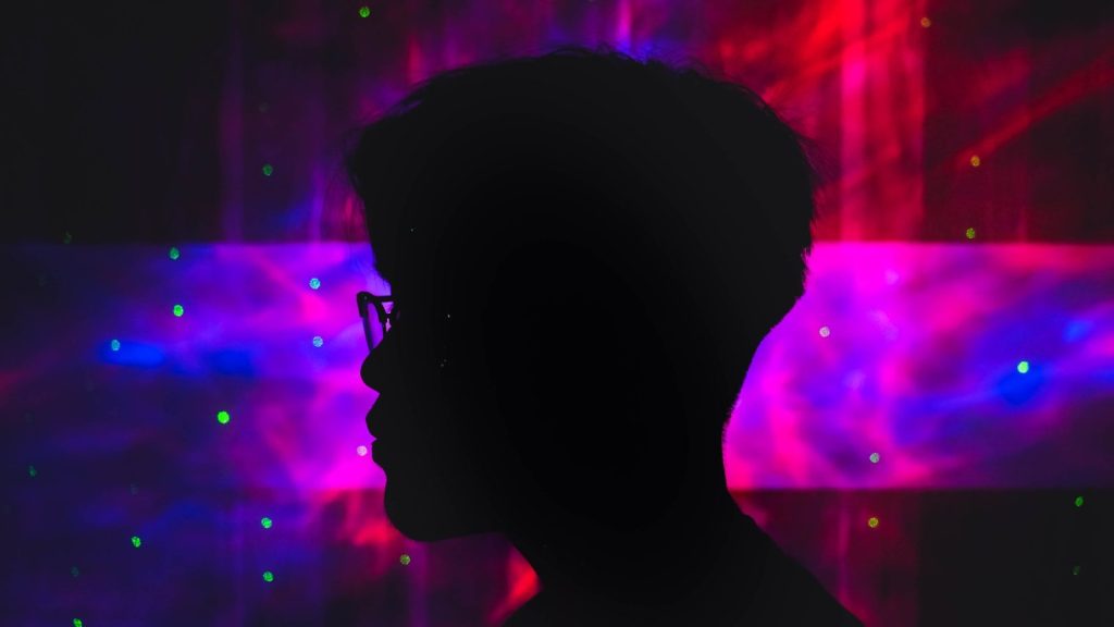 a silhouette of a man with glasses in front of a colorful background