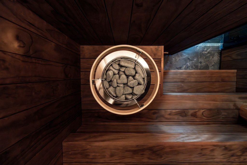 A modern sauna heater with stones in a wooden room.