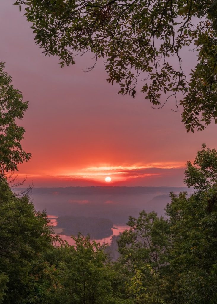 the sun is setting over a valley with trees