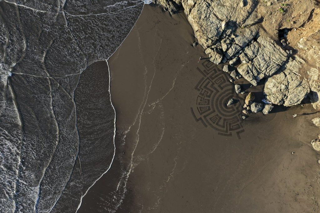 Sand maze art on beach with ocean waves