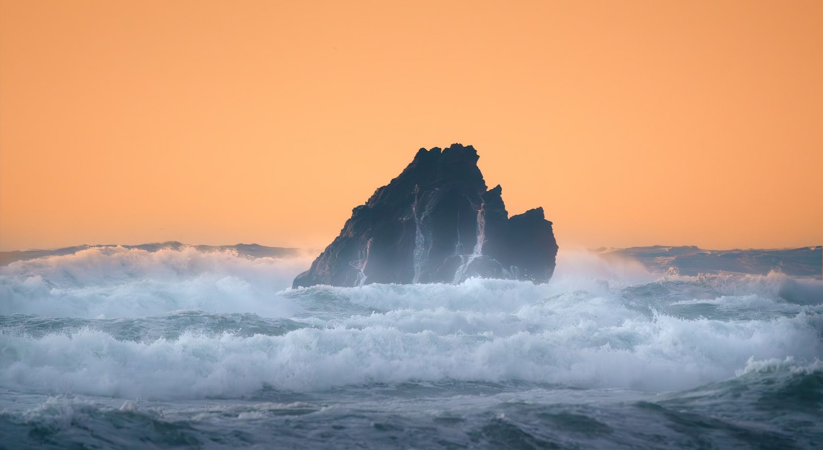 Jagged rock formation emerges from stormy ocean waves