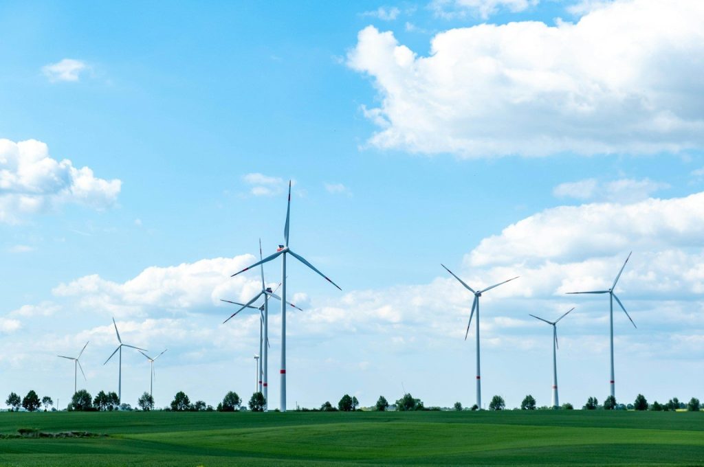 Green field with wind turbines under a cloudy blue sky.
