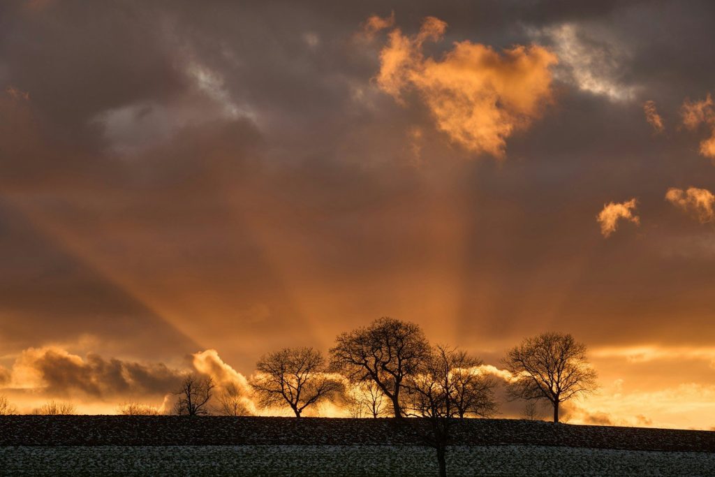 The sun is shining through the clouds over a field