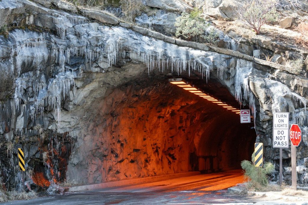 Icicles hang from a rock tunnel entrance with orange light.