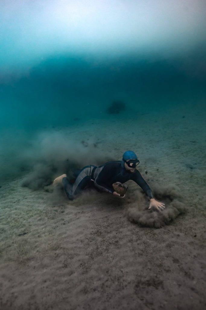Man free-diving on sandy ocean floor stirring up sediment.