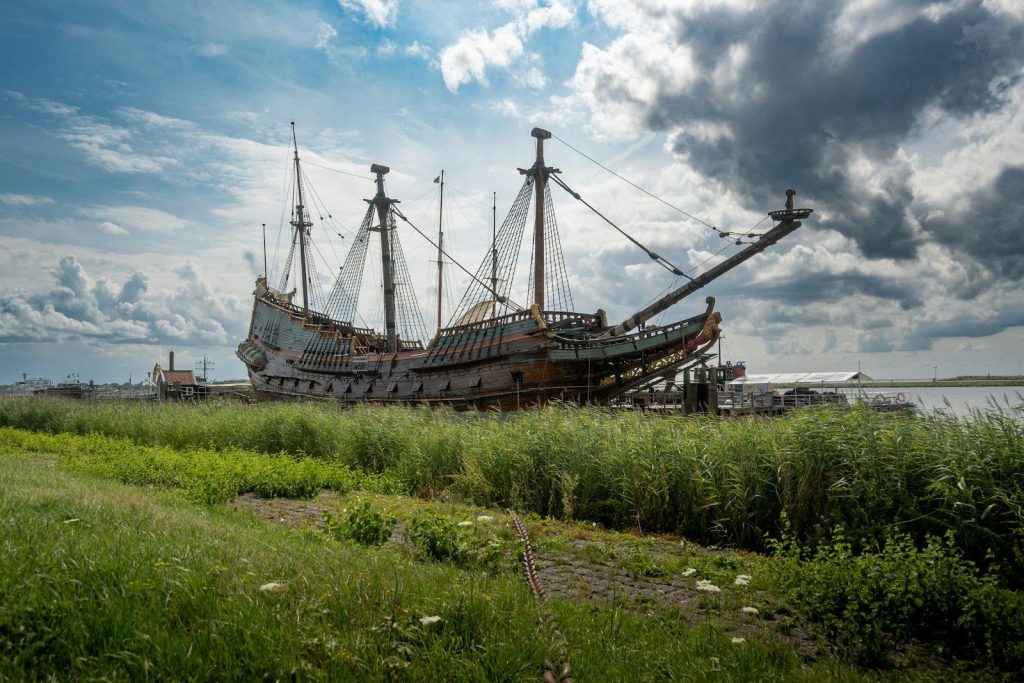 A large historic sailing ship docked by a grassy shore.